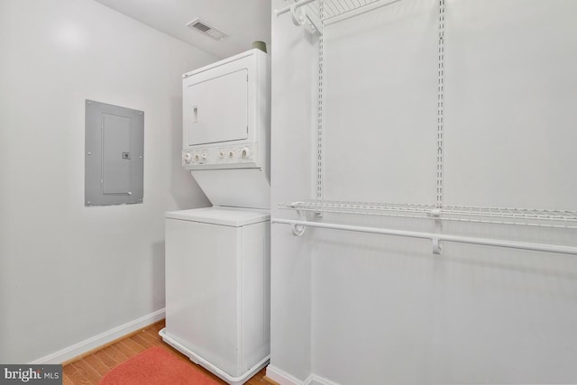 laundry room with hardwood / wood-style flooring, electric panel, and stacked washer and clothes dryer