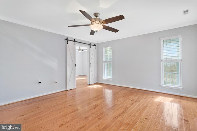 empty room featuring crown molding, plenty of natural light, a barn door, and light wood-type flooring