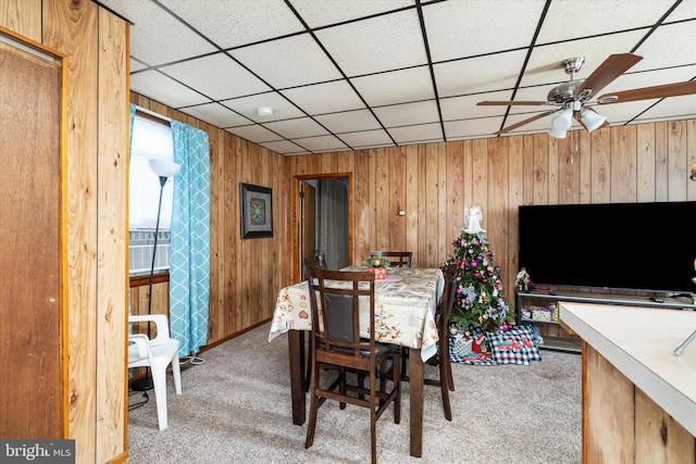 dining space featuring ceiling fan, wood walls, a drop ceiling, and light carpet