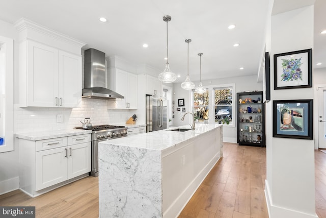 kitchen featuring wall chimney range hood, a kitchen island with sink, white cabinets, and premium appliances