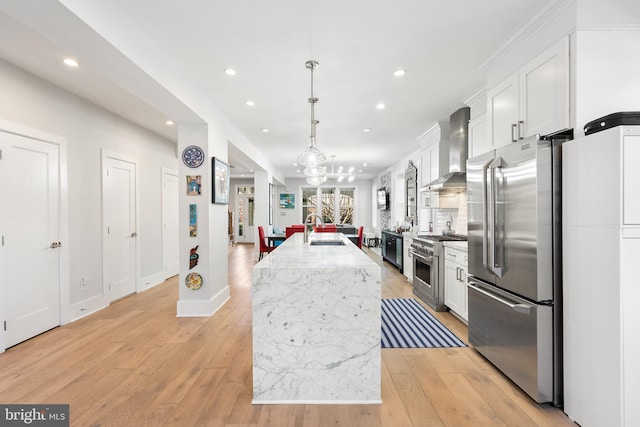 kitchen featuring premium appliances, pendant lighting, wall chimney exhaust hood, white cabinetry, and a center island with sink