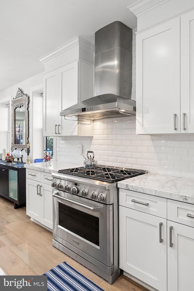 kitchen featuring high end range, light hardwood / wood-style floors, tasteful backsplash, white cabinetry, and wall chimney range hood