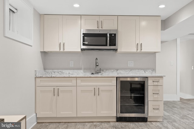 kitchen with sink, light wood-type flooring, light stone countertops, and beverage cooler