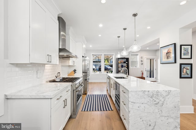 kitchen with appliances with stainless steel finishes, white cabinetry, wall chimney range hood, decorative light fixtures, and sink