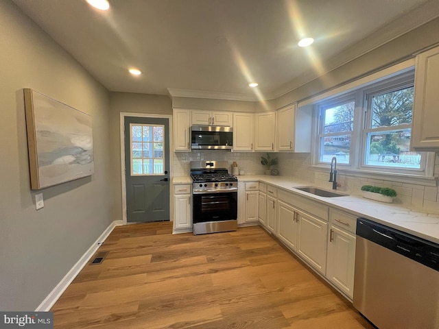 kitchen with ornamental molding, stainless steel appliances, sink, light hardwood / wood-style flooring, and white cabinets