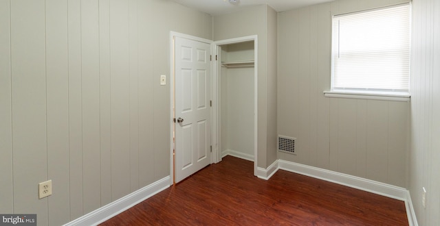 unfurnished bedroom with dark hardwood / wood-style flooring, wooden walls, and a closet