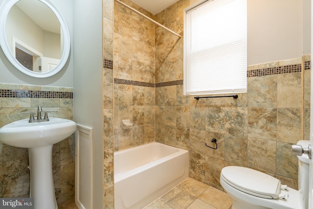 bathroom with tiled shower / bath combo, toilet, and tile walls