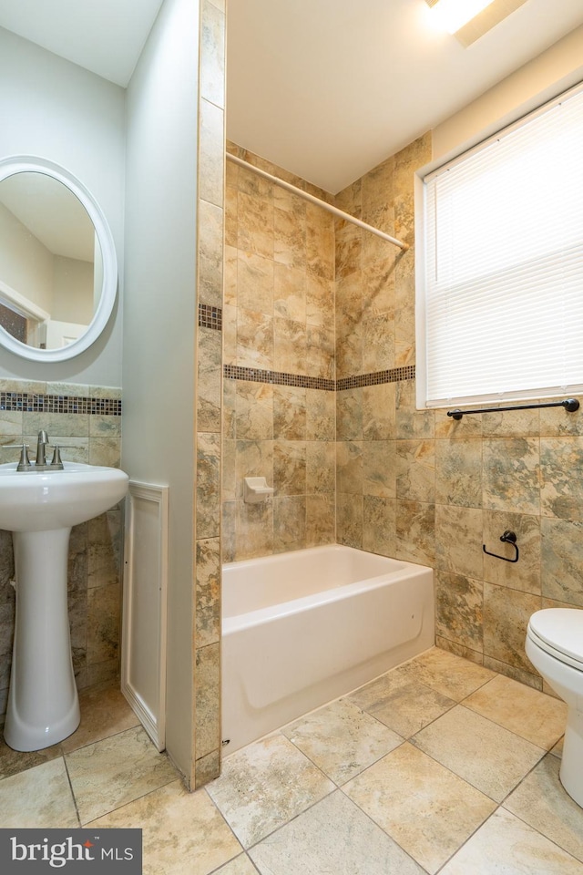 bathroom with toilet, tile walls, and tiled shower / bath