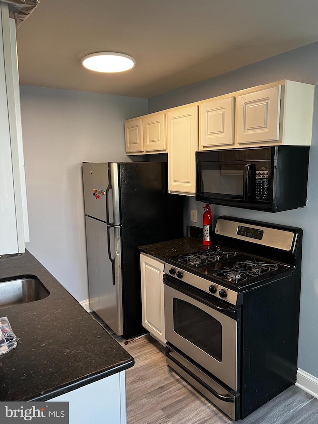 kitchen featuring dark stone counters, stainless steel appliances, sink, white cabinets, and light hardwood / wood-style floors