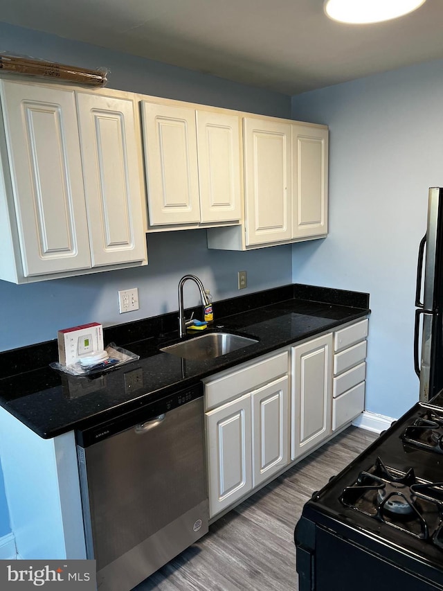 kitchen with white cabinetry, sink, stainless steel appliances, dark stone countertops, and light wood-type flooring