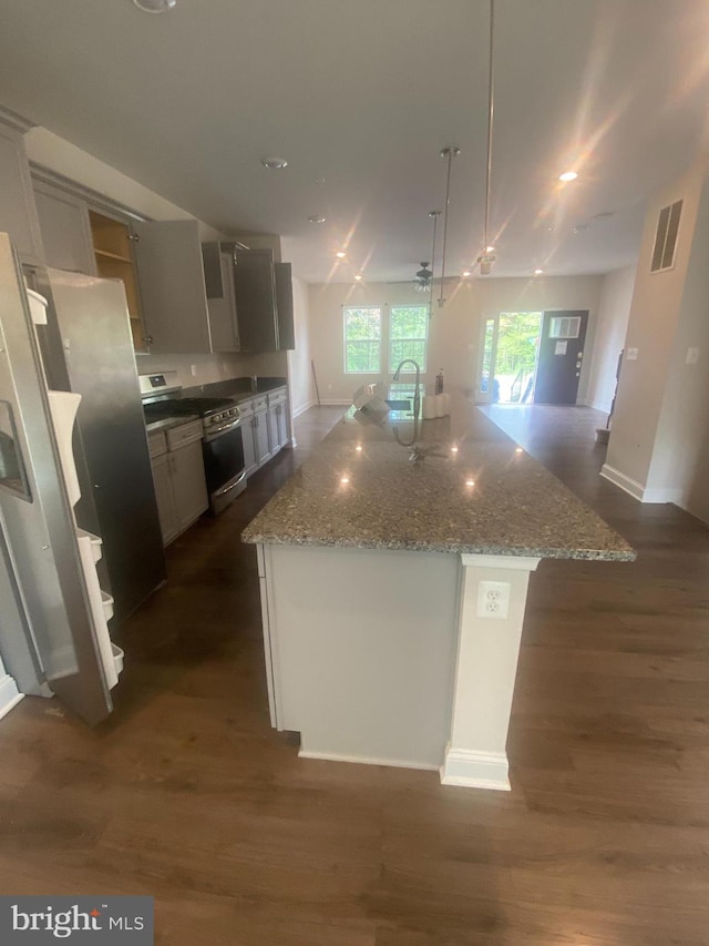 kitchen with light stone counters, an island with sink, dark wood-type flooring, and decorative light fixtures