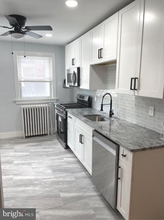 kitchen featuring white cabinets, appliances with stainless steel finishes, radiator heating unit, and sink