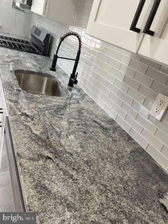 room details featuring decorative backsplash, sink, stone countertops, white cabinets, and range