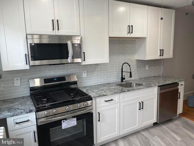 kitchen featuring sink, light hardwood / wood-style flooring, decorative backsplash, white cabinets, and appliances with stainless steel finishes