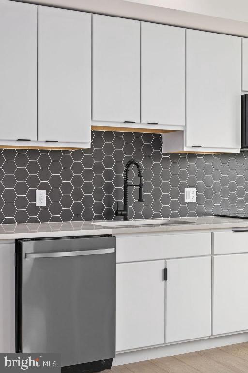 kitchen featuring stainless steel dishwasher, decorative backsplash, and white cabinetry