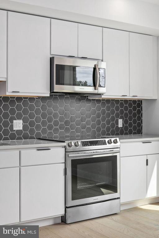 kitchen with tasteful backsplash, white cabinets, light wood-type flooring, and appliances with stainless steel finishes