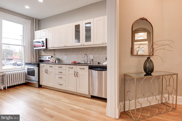 kitchen featuring radiator heating unit, white cabinets, stainless steel appliances, and light hardwood / wood-style floors