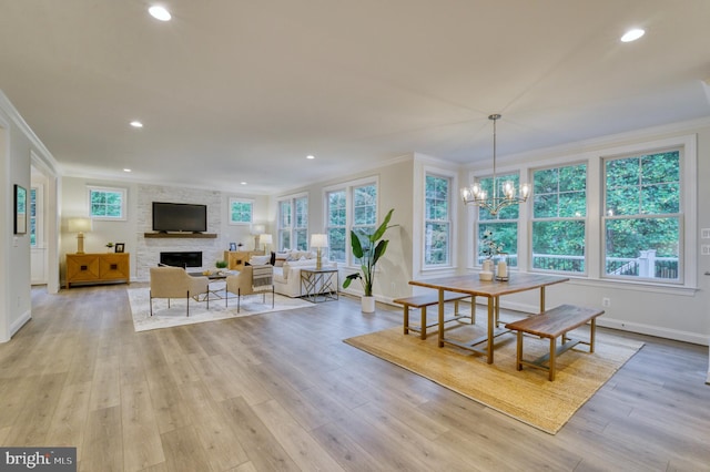 dining space featuring a fireplace, an inviting chandelier, crown molding, and light hardwood / wood-style flooring