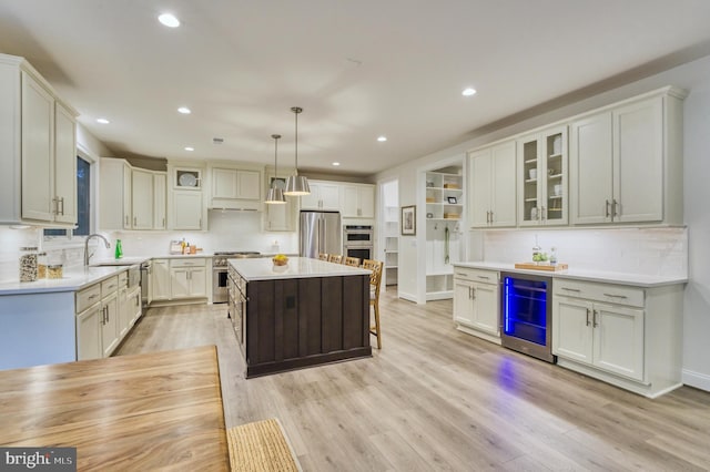 kitchen with a center island, stainless steel appliances, wine cooler, pendant lighting, and light hardwood / wood-style floors