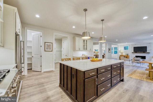 kitchen featuring light wood-type flooring, dark brown cabinetry, a large fireplace, decorative light fixtures, and white cabinets