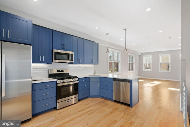 kitchen featuring sink, kitchen peninsula, decorative light fixtures, appliances with stainless steel finishes, and light wood-type flooring