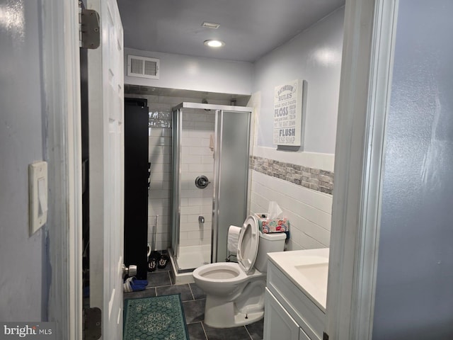 bathroom with tile patterned floors, toilet, vanity, a shower with shower door, and tile walls