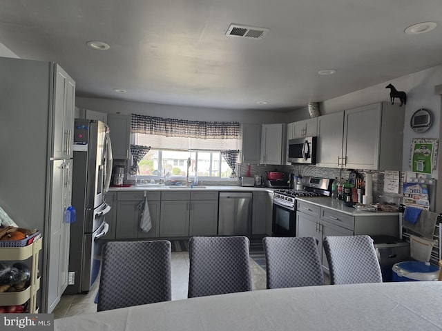 kitchen with appliances with stainless steel finishes, backsplash, gray cabinets, and light tile patterned floors