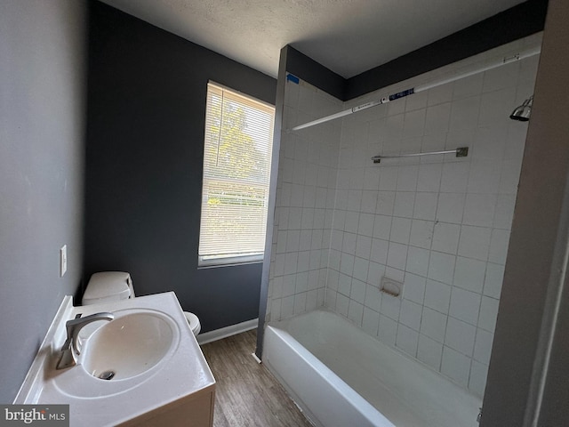 full bathroom featuring vanity, tiled shower / bath, hardwood / wood-style flooring, toilet, and a textured ceiling