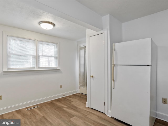 kitchen featuring white fridge, light wood-type flooring, and a textured ceiling