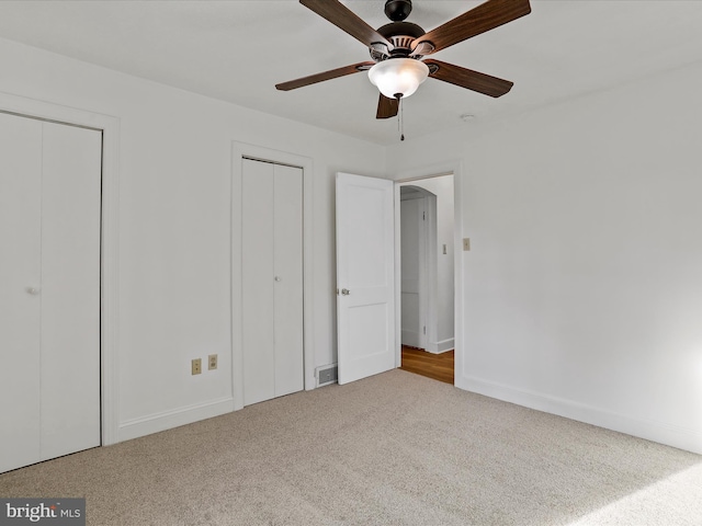 unfurnished bedroom with ceiling fan, carpet floors, and two closets