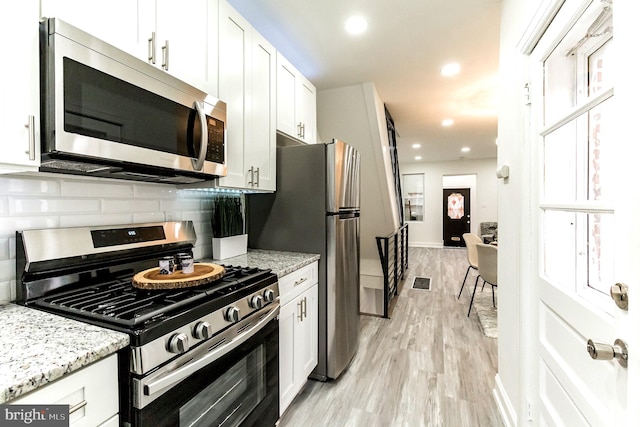 kitchen with white cabinetry, stainless steel appliances, tasteful backsplash, light stone counters, and light wood-type flooring