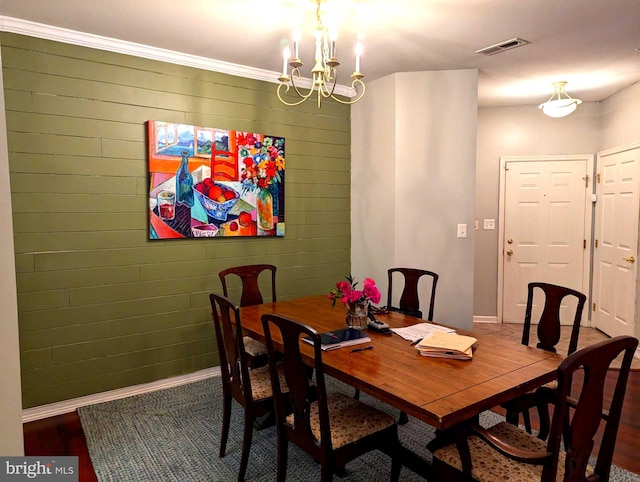 dining room featuring wood walls, ornamental molding, and an inviting chandelier