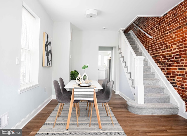 dining space with dark hardwood / wood-style flooring and brick wall