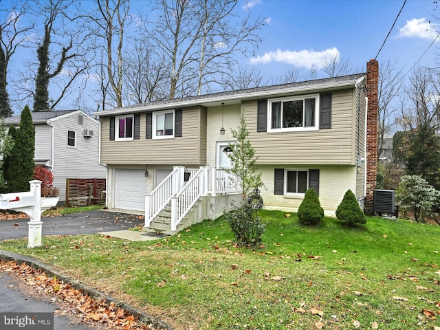 bi-level home featuring central AC unit, a front yard, and a garage