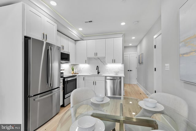 kitchen with white cabinetry, sink, stainless steel appliances, and light hardwood / wood-style floors