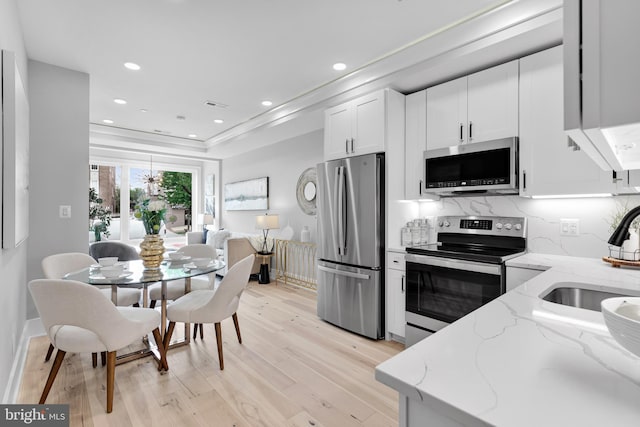 kitchen featuring light stone counters, light hardwood / wood-style flooring, backsplash, white cabinets, and appliances with stainless steel finishes