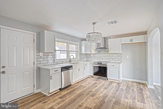 kitchen with white cabinets, wall chimney exhaust hood, sink, and appliances with stainless steel finishes