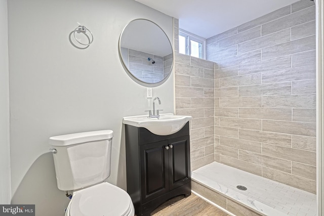 bathroom with a tile shower, vanity, toilet, and hardwood / wood-style floors