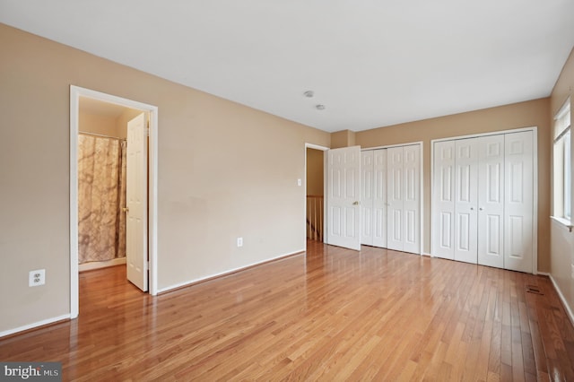 unfurnished bedroom with ensuite bathroom, light hardwood / wood-style floors, and two closets