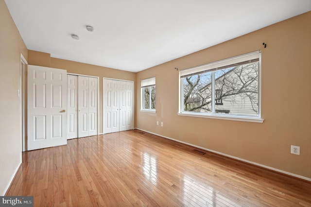 unfurnished bedroom featuring light hardwood / wood-style floors and multiple closets