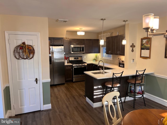 kitchen with sink, appliances with stainless steel finishes, decorative light fixtures, a kitchen bar, and kitchen peninsula