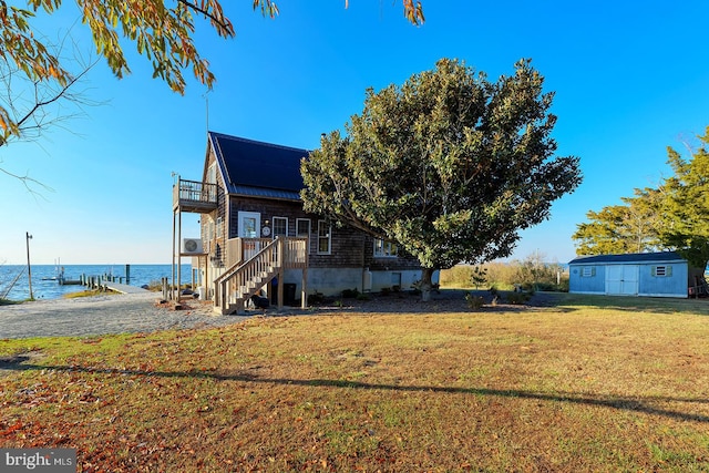 view of home's exterior featuring a boat dock, a yard, a water view, and a shed