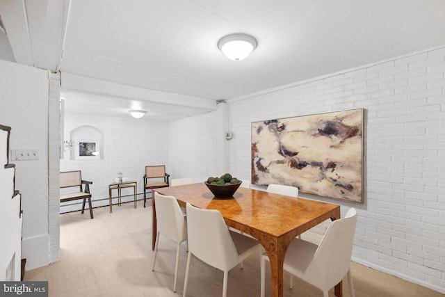 dining area featuring light hardwood / wood-style floors, a baseboard radiator, and brick wall