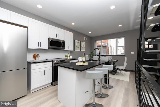 kitchen featuring sink, light hardwood / wood-style flooring, an island with sink, appliances with stainless steel finishes, and white cabinetry