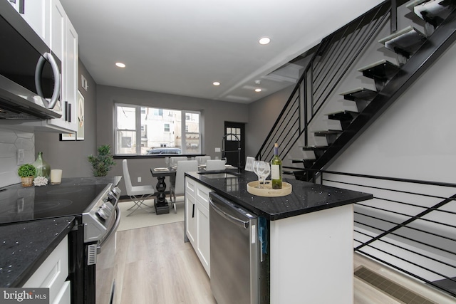 kitchen with appliances with stainless steel finishes, light hardwood / wood-style flooring, dark stone countertops, white cabinets, and a center island