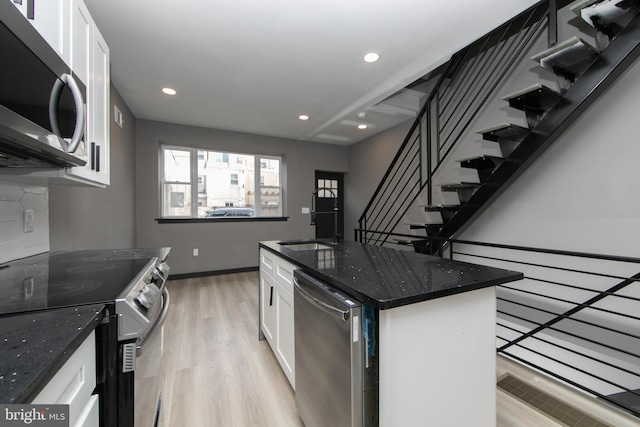 kitchen with white cabinets, appliances with stainless steel finishes, dark stone counters, a kitchen island, and light wood-type flooring