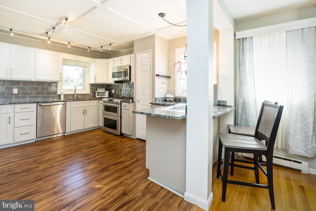 kitchen with white cabinets, dark hardwood / wood-style floors, kitchen peninsula, and stainless steel appliances