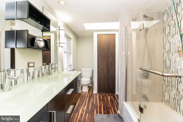 full bathroom with hardwood / wood-style flooring, vanity, toilet, and bath / shower combo with glass door