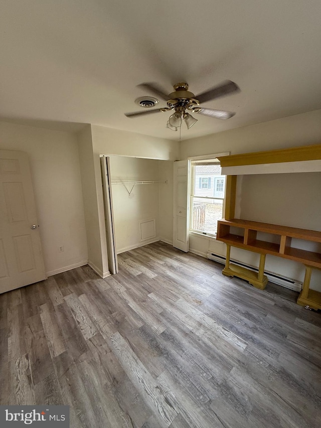 unfurnished bedroom featuring baseboard heating, a closet, light hardwood / wood-style flooring, and ceiling fan