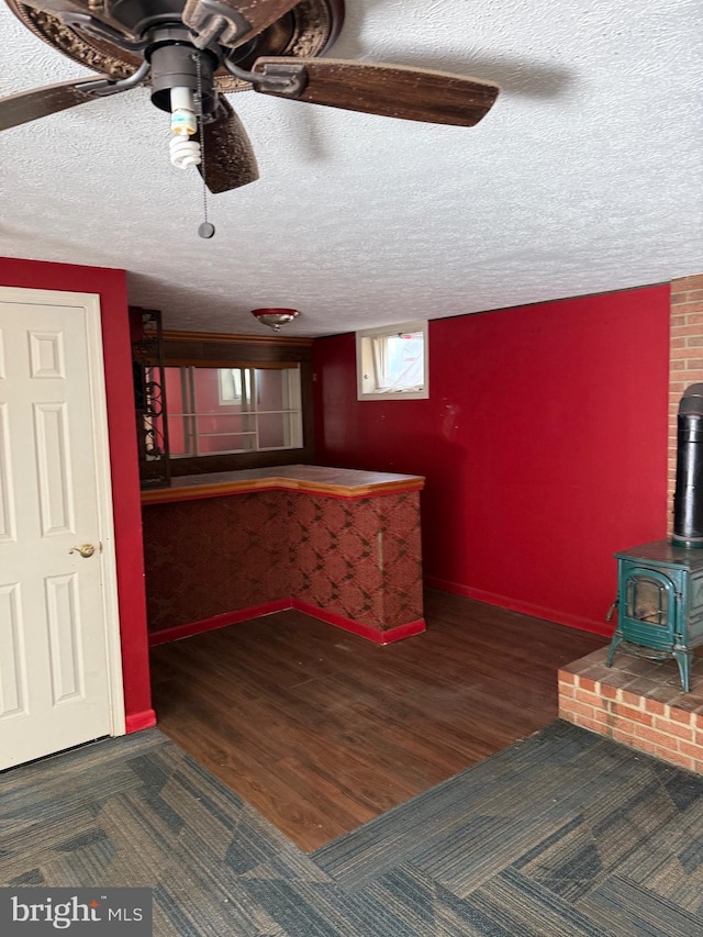 bar featuring a textured ceiling, dark hardwood / wood-style flooring, a wood stove, and ceiling fan